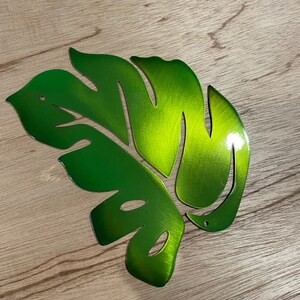 Puede incluir: Una hoja de metal verde con un dise&ntilde;o de corte. La hoja es brillante y tiene un acabado de metal cepillado.