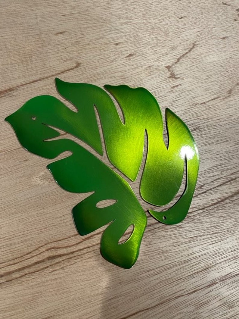 Puede incluir: Una hoja de metal verde con un dise&ntilde;o de corte. La hoja es brillante y tiene un acabado de metal cepillado.