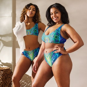 May include: Two women wearing matching blue and green patterned swimsuits. The swimsuit top is a halter style and the bottom is a high-waisted bikini bottom.