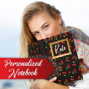 May include: A black personalized notebook with a cherry pattern and a gold frame with the name "Kate" written in white. The notebook is being held by a person.