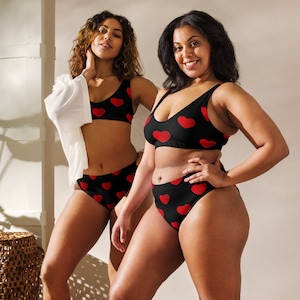 May include: Two women wearing black and red heart print lingerie. The lingerie includes a bra and high-waisted underwear.