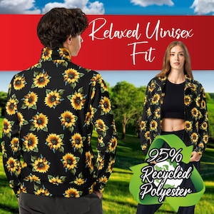 Peut inclure: Veste noire à imprimé tournesol. La veste a une fermeture éclair et des manches longues. Le texte "Relaxed Unisex Fit" et "95% Recycled Polyester" est visible sur l'image.