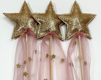 May include: Three gold glitter star wands with pink tulle and gold glitter stars. The wands are made of wood and have a pink tulle ribbon attached to them.