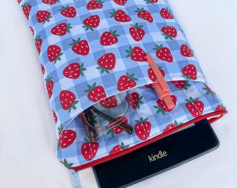 Könnte beinhalten: Eine gesteppte Stoffhülle mit blauem Vichy-Muster und roten Erdbeeren. Die Hülle hat einen roten Reißverschluss und enthält ein Kindle, eine Brille und einen rosa Stift. Ein Erdbeer-Anhänger hängt am Reißverschluss.