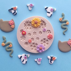 May include: A silicone mould with 16 different shapes, including flowers, cats, snakes, and cows. The mould is pink and has a white background. The mould is filled with colourful polymer clay shapes.