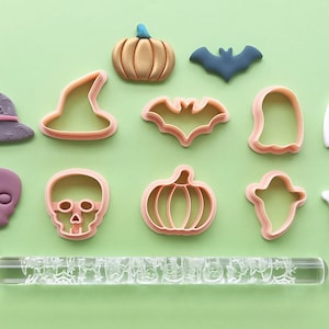 May include: A set of Halloween-themed cookie cutters, including a witch's hat, a pumpkin, a bat, a ghost, and a skull. There is also a rolling pin with a Halloween design.