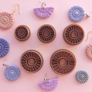 May include: A set of four brown plastic cookie cutters in the shape of a sunburst, with a smaller circle in the centre.  There are also several pairs of earrings with a sunburst design in pink, purple, and blue.