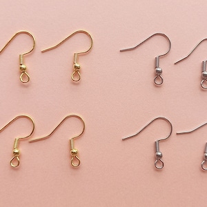May include: Six earring hooks, three gold and three silver, on a pink background. The hooks are all the same size and shape, with a small loop at the top and a small ball at the bottom.