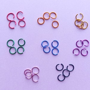 May include: Assortment of jump rings in various colors, including red, orange, green, blue, and purple. The jump rings are arranged in groups of four or five.