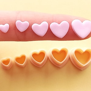 May include: A set of six heart-shaped cookie cutters in various sizes. The cutters are made of pink plastic and are arranged in order of size, with the smallest cutter on the left and the largest cutter on the right.