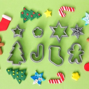 May include: A collection of Christmas-themed cookie cutters and decorations, including gingerbread men, candy canes, stockings, snowflakes, stars, and Christmas trees. The items are arranged on a green background.