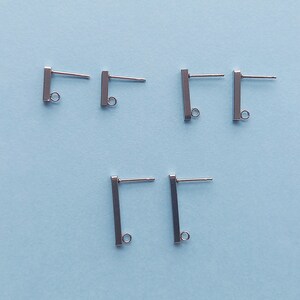 May include: Five silver earring posts with a small loop at the bottom. The posts are rectangular in shape.