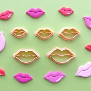 May include: A set of 10 pink and beige plastic cookie cutters shaped like lips. The cutters are arranged on a green background.