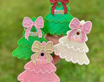 Könnte beinhalten: Eine Auswahl an Weihnachtsbaumschmuck in Grün, Rosa und Weiß. Jeder Baumschmuck hat eine glitzernde Schleife und den Text "MERAKI CREATIONS". Die Ornamente werden vor einem verschwommenen grünen Hintergrund präsentiert.