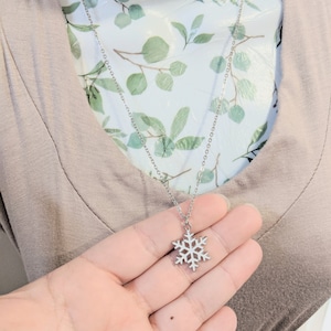 May include: A silver snowflake pendant necklace on a silver chain. The necklace is displayed on a mannequin with a floral pattern.