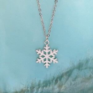 May include: A silver chain necklace with a white snowflake pendant. The snowflake is a simple design with six points.