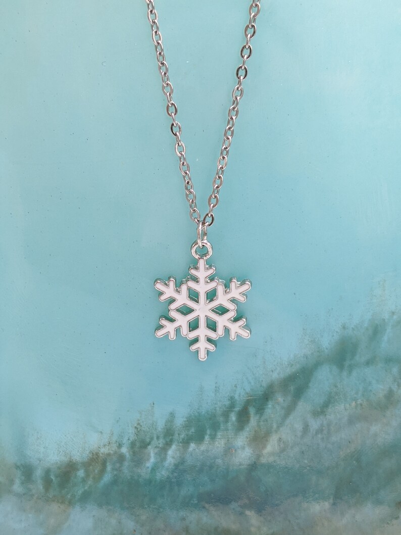 May include: A silver chain necklace with a white snowflake pendant. The snowflake is a simple design with six points.