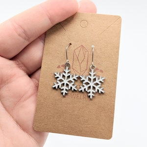 May include: Silver snowflake dangle earrings on a brown card with the word "jewelry" printed on it.