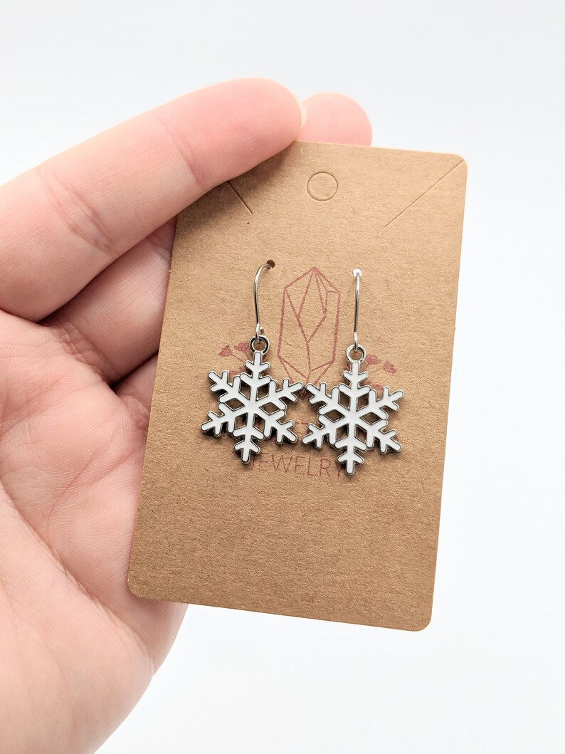 May include: Silver snowflake dangle earrings on a brown card with the word "jewelry" printed on it.