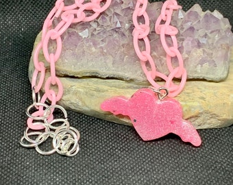 May include: A pink plastic chain necklace with a pink glitter heart pendant with wings.