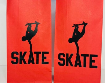 May include: Two red paper gift bags with blue tissue paper inside. Each bag has a black silhouette of a skateboarder with the word "SKATE" printed below.