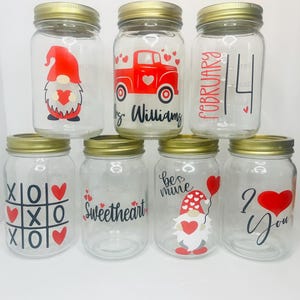 May include: Seven glass jars with gold lids decorated with Valentine's Day themes. The jars feature designs such as a gnome, a red truck, a heart, the words "Sweetheart", "Be Mine", "I Love You", and "February 14".