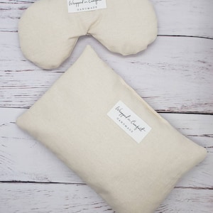 May include: Two beige fabric eye pillows with the text "Wrapped in Comfort Handmade" on the label.