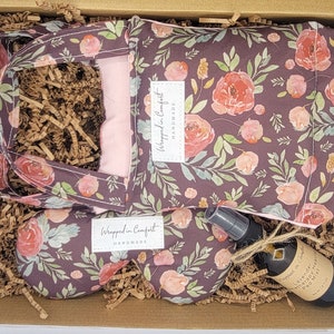 May include: A gift box filled with brown paper shred and three items: a floral print tote bag, a floral print eye pillow, and a small bottle of lavender aromatherapy spray. The tote bag and eye pillow have the text "Wrapped in Comfort Handmade" on them.