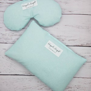 May include: Two light blue fabric eye pillows with the text "Wrapped in Comfort Handmade" on the front.
