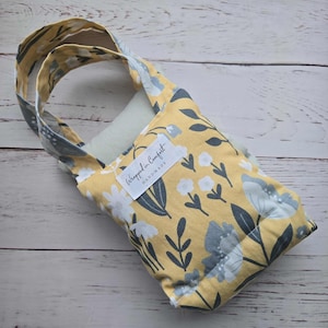 Könnte beinhalten: Eine handgefertigte florale Tragetasche. Die Tasche hat einen gelben Hintergrund mit einem Muster aus grauen und weißen Blumen und Blättern. Sie hat eine rechteckige Form mit einem Griff und einem Etikett mit der Aufschrift "Wrapped in Comfort Handmade."