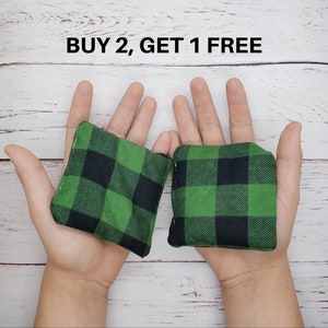 May include: Two green and black checked bean bags, held in the hands of a person. The text "BUY 2, GET 1 FREE" is displayed above the bean bags.