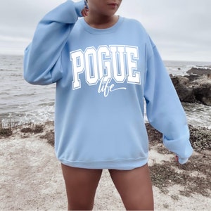 Puede incluir: Una sudadera azul claro con el texto "POGUE life" en blanco.