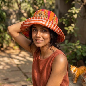 Peut inclure: Un chapeau à larges bords avec un motif rayé orange et rose vif. Le chapeau présente un imprimé tigre sur le dessus et un bord rayé. Un accessoire de mode.