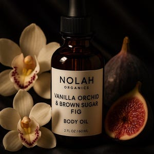 May include: A dark amber glass bottle of Nolah Organics Vanilla Orchid & Brown Sugar Fig Body Oil, 60 ml, with a black dropper. The bottle is surrounded by white orchid flowers and figs.