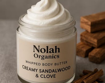 Może przedstawiać: Szklany słoik z ubijanym masłem do ciała Nolah Organics w aromacie Creamy Sandalwood & Clove. Słoik znajduje się na jasnobrązowej powierzchni, wokół której rozrzucone są goździki i patyczki sandałowe.