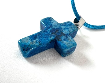 May include: A blue stone cross pendant with a matching blue cord. The cross is a vibrant blue with darker blue and gray marbling. The cord is attached to the cross with a silver-colored metal clasp.