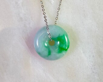 May include: A jade pendant necklace with a green and white jade donut pendant on a silver chain.