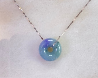 May include: A silver chain necklace with a light blue and purple jade pendant in the shape of a donut.
