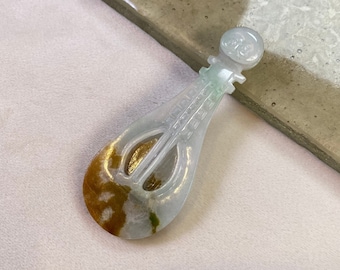 Puede incluir: Una talla de violín de jade blanco con detalles dorados. La talla está sobre una superficie gris claro.