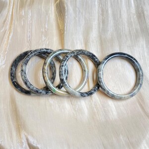 May include: Five jade bangles with a black and white marbled pattern. The bangles are stacked on top of each other.
