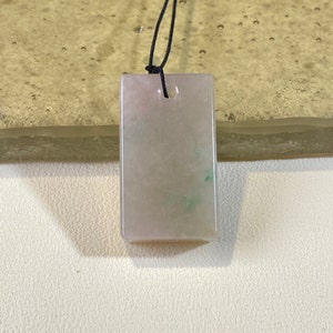 Könnte beinhalten: Ein rechteckiger Jade-Anhänger in hellgrüner und weißer Farbe. Der Anhänger hat oben ein Loch für eine Schnur oder Kette.