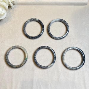 May include: Five jade bangles with a mottled black and white pattern. The bangles are arranged in a semi-circle on a white surface.
