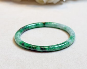 May include: A jade bangle bracelet in shades of green. The polished surface of the bracelet reflects light, highlighting the natural patterns within the stone. This elegant piece of jewellery is a classic accessory, suitable for everyday wear.