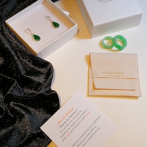 May include: A white box with the text "GRANSKY JEWELLERY" on the lid. Inside the box are two green jade rings. A white box with the text "GRANSKY JEWELLERY" on the lid. Inside the box are two green jade earrings. A white card with the text "Love our Customer" and a message about the company's commitment to customer service.