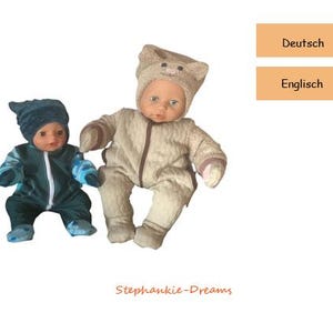 Könnte beinhalten: Zwei Babypuppen in Winteroutfits. Eine Puppe trägt einen dunkelblauen Overall mit passendem Hut und blauen Akzenten. Die andere Puppe trägt einen beigefarbenen Overall mit einem bärenförmigen Hut. Die Puppen stehen vor weißem Hintergrund.