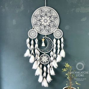 Op de afbeelding: Witte droomvanger met een groot cirkelvormig macramé-ontwerp, een halve maan en een ster. De droomvanger is versierd met witte veren.