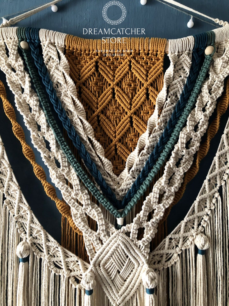 May include: A macrame wall hanging with a geometric design in beige, mustard yellow, teal, and dark blue. The hanging features a variety of knots and tassels.