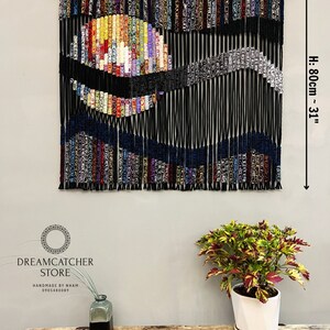May include: A colorful macrame wall hanging with a black background and a large, colorful circle in the center. The hanging is 40 inches wide and 31 inches tall.