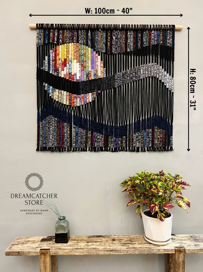 May include: A colorful macrame wall hanging with a black background and a large, colorful circle in the center. The hanging is 40 inches wide and 31 inches tall.