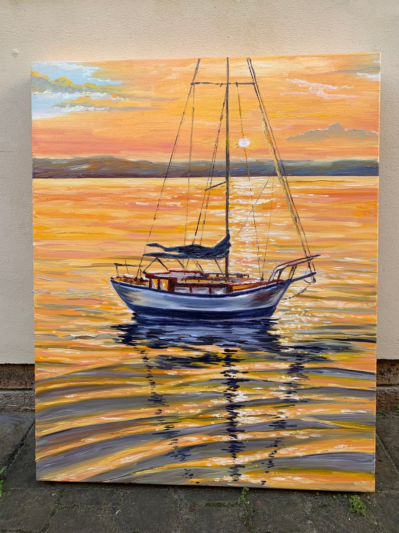 May include: A sailboat with white sails and a blue hull is anchored in a calm body of water. The sun is setting, casting a warm orange glow on the water and sky. The sailboat's reflection is visible in the water.